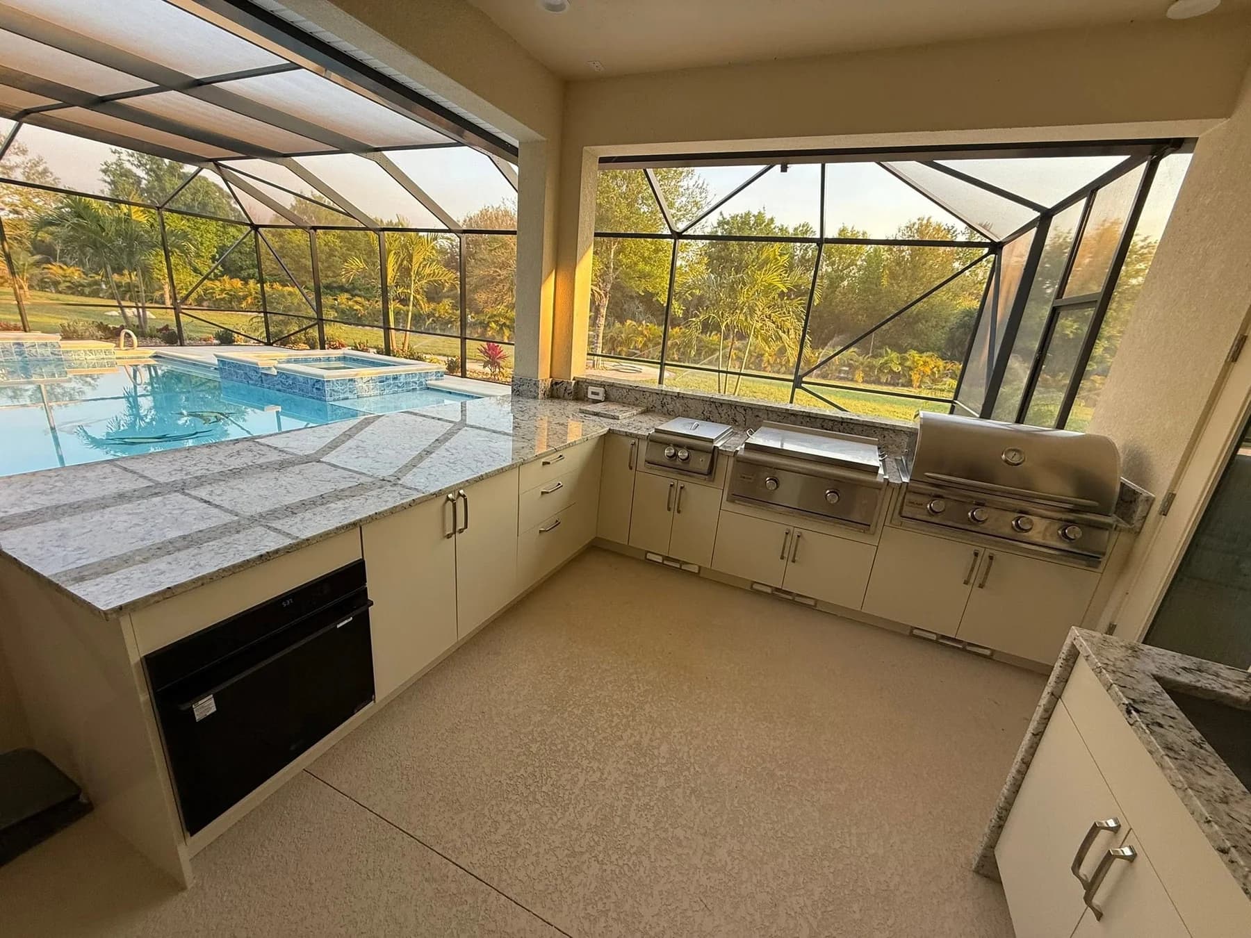Completed outdoor kitchen with light-colored cabinetry, cooking appliances, and a poolside view